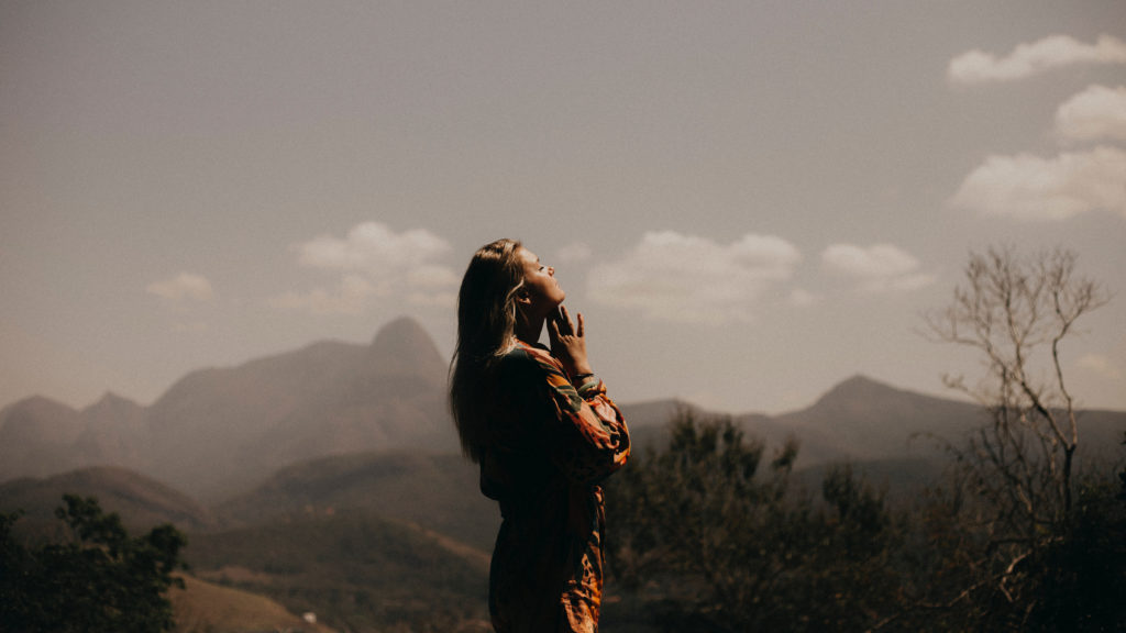 A young woman stands contemplatively looking out over the mountains as she learns how to overcome anxious thoughts.
